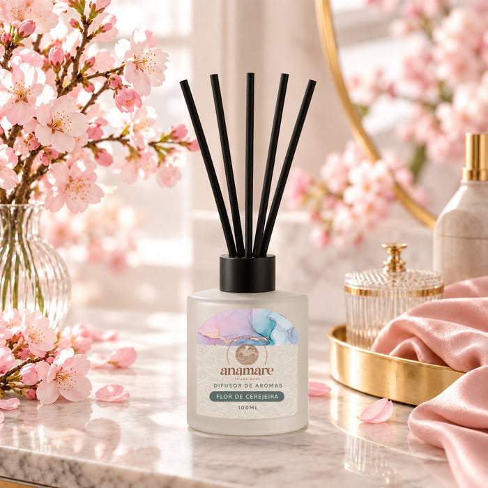 Difusor de Aromas Flor de Cerejeira 100 mL, frasco de vidro fosco com varetas pretas, em bancada de mármore com galhos de flor de cerejeira