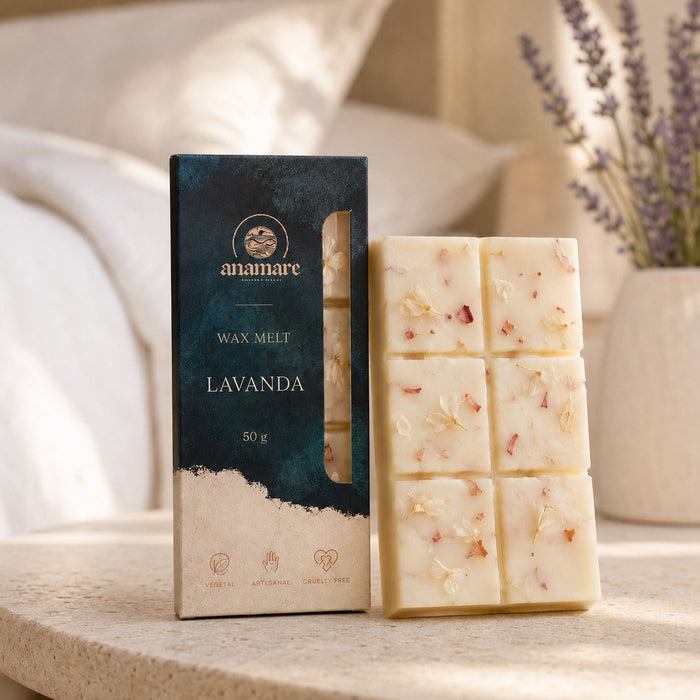 Wax Melt Anamare Lavanda de 50 g, barra de cera vegetal com pétalas secas ao lado da caixa azul-petróleo com janela, em cabeceira de cama com roupa de cama branca e lavandas em vaso de cerâmica, sobre mesa lateral de travertino