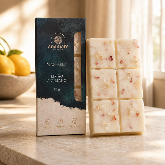 Wax Melt Anamare Limão Siciliano de 50 g, barra de cera vegetal com pétalas secas ao lado da caixa azul-petróleo com janela, em cozinha em luz filtrada por cortina de voil, com limões sicilianos em bowl de pedra sobre bancada de travertino
