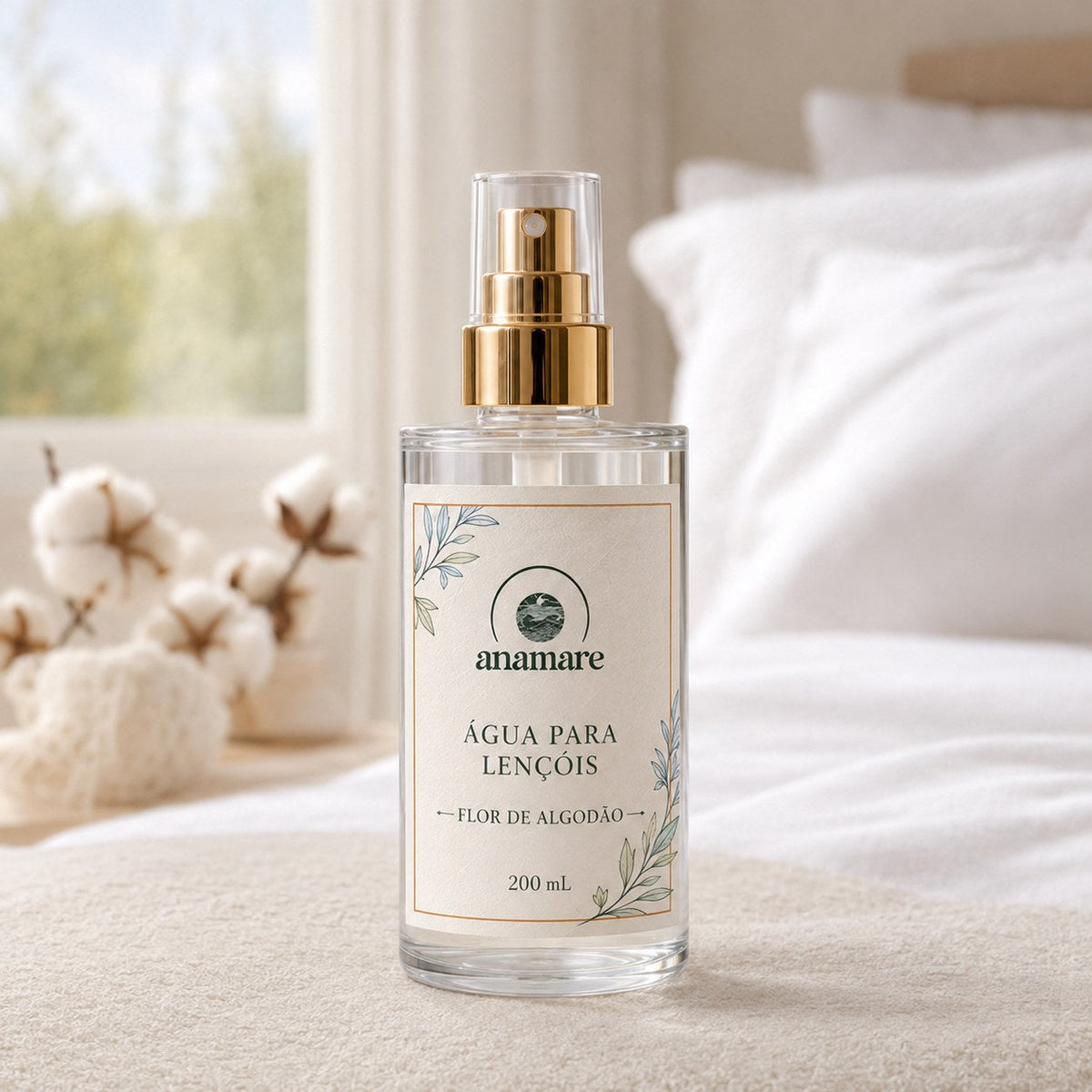 Água de Lençóis Anamare Flor de Algodão, frasco de vidro de 200 mL com válvula spray dourada e rótulo cru, em quarto claro com roupa de cama branca e ramos de algodão