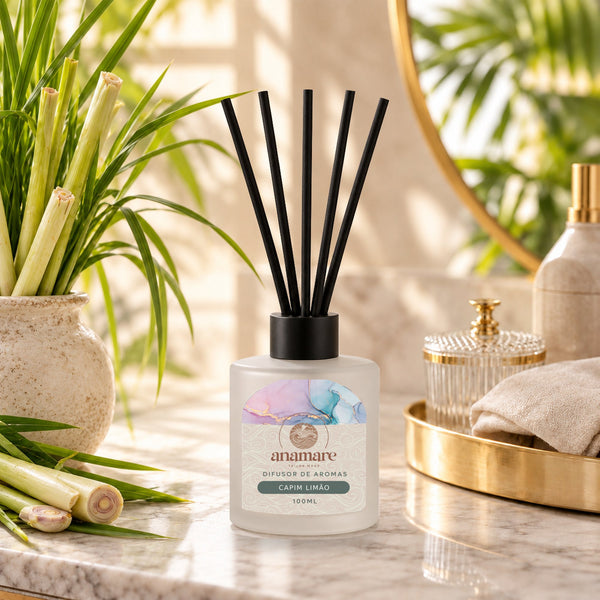 Difusor de Aromas Capim Limão 100 mL, frasco de vidro fosco com varetas pretas, em bancada de mármore com talos de capim-limão em vaso de cerâmica