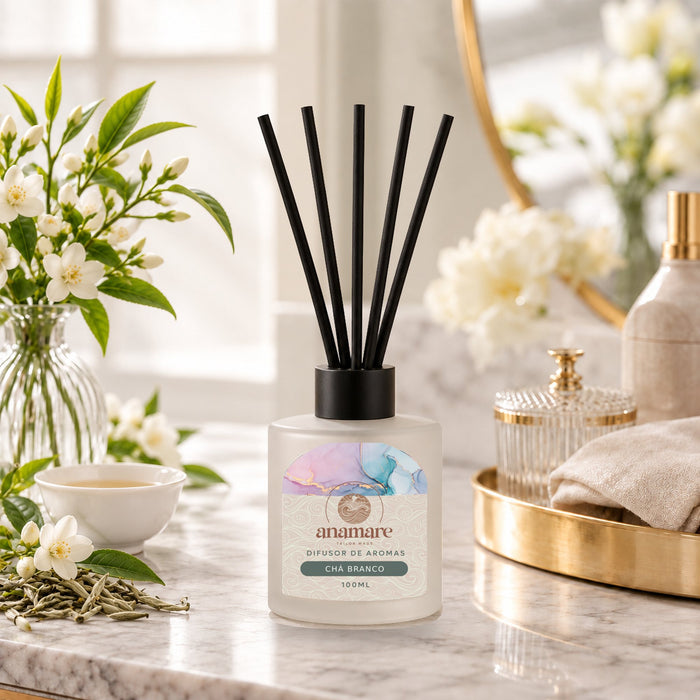 Difusor de Aromas Chá Branco 100 mL, frasco de vidro fosco com varetas pretas, em bancada de mármore com flores de chá e uma xícara