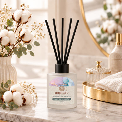 Difusor de Aromas Flor de Algodão 100 mL, frasco de vidro fosco com varetas pretas, em bancada de mármore com flores de algodão e eucalipto