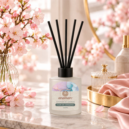 Difusor de Aromas Flor de Cerejeira 100 mL, frasco de vidro fosco com varetas pretas, em bancada de mármore com galhos de flor de cerejeira