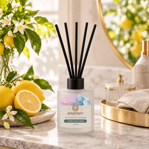 Difusor de Aromas Limão Siciliano 100 mL, frasco de vidro fosco com varetas pretas, em bancada de mármore com limões sicilianos e flores de laranjeira