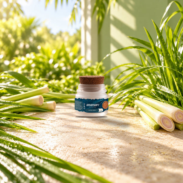 Vela aromática Petit 25 g Capim Limão sobre bancada de pedra, entre talos e folhas de capim-limão