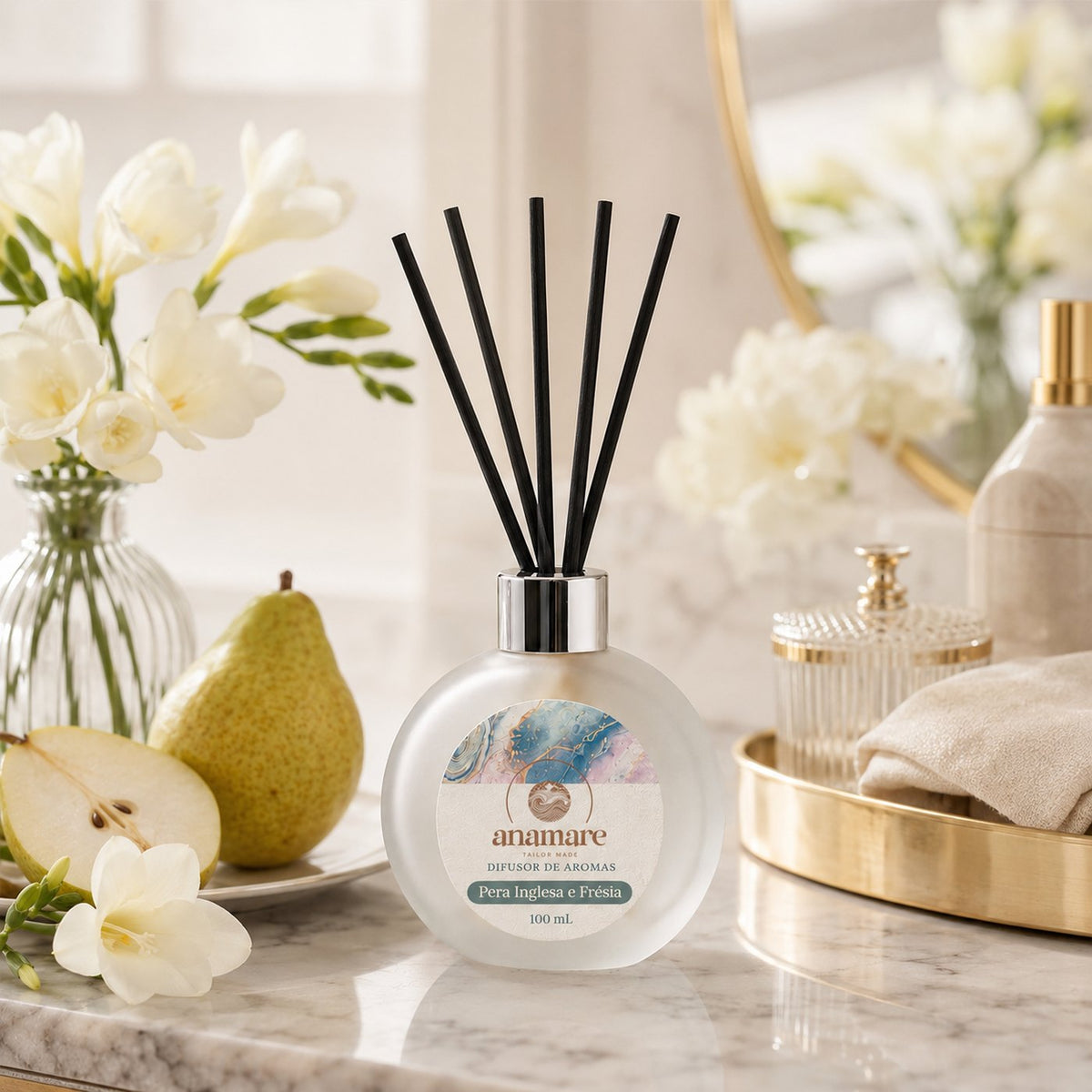 Difusor de Aromas Anamare Pera Inglesa e Frésia de 100 mL, frasco redondo de vidro fosco com tampa cromada e varetas pretas, em composição delicada de tons claros e rosados, sobre superfície lisa