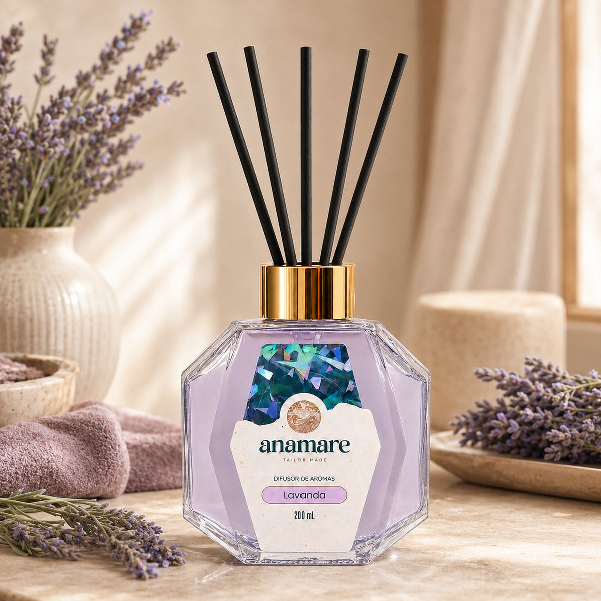 Difusor de Aromas Anamare Lavanda de 200 mL, frasco octogonal facetado de vidro com tampa dourada e varetas pretas, em bancada de pedra clara, com lavanda fresca em vaso de cerâmica canelado, toalha lilás e pires com ramos secos, em luz de janela