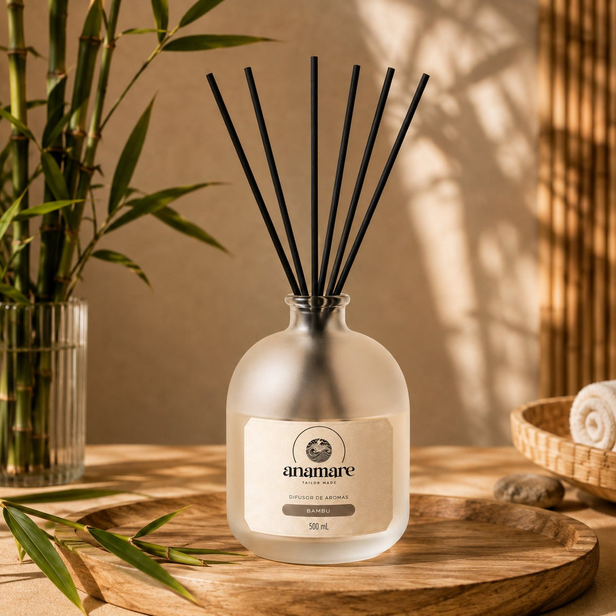 Difusor de Aromas Anamare Bambu de 500 mL, frasco de vidro fosco de ombro alto com gargalo prateado e varetas pretas, em bandeja redonda de madeira, com bambu em vaso de vidro canelado, seixo e toalha enrolada em cesto