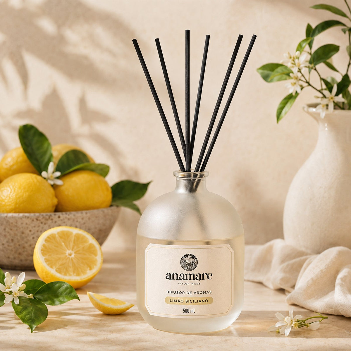 Difusor de Aromas Anamare Limão Siciliano de 500 mL, frasco de vidro fosco de ombro alto com gargalo prateado e varetas pretas, em cena clara e cítrica, sobre superfície lisa com fundo neutro