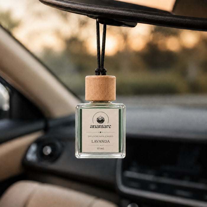 Difusor de Carro Anamare Lavanda, frasco de vidro quadrado de 10 mL com tampa de madeira e cordão preto, pendurado no retrovisor de um carro, com o painel desfocado e luz de fim de tarde pela janela