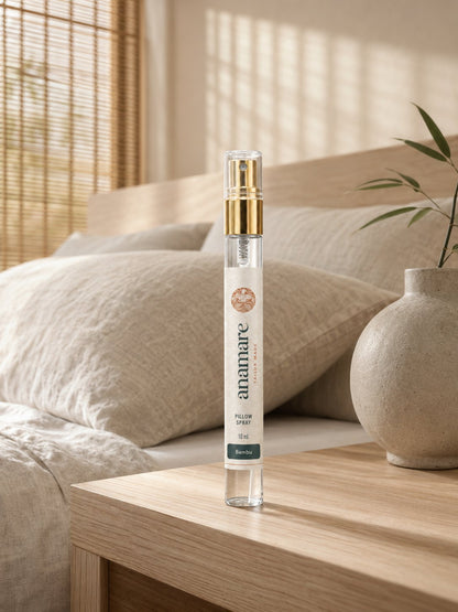 Pillow Spray Bambu 10 mL, flaconete de vidro com válvula spray dourada, em mesa de madeira clara, com haste de bambu em vaso de cerâmica e persiana de bambu filtrando o sol