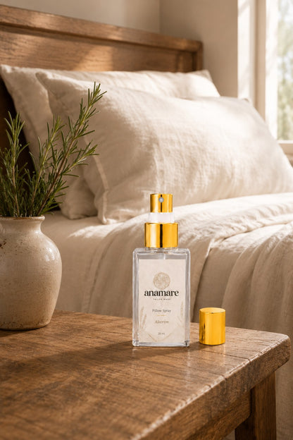Pillow Spray Alecrim 30 mL, frasco de vidro com válvula e tampa douradas, em quarto rústico com roupa de cama de linho cru e alecrim fresco em vaso de cerâmica, sobre mesa de madeira envelhecida