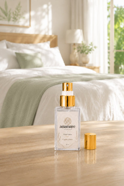 Pillow Spray Capim Limão 30 mL, frasco de vidro com válvula e tampa douradas, em quarto arejado com manta verde-sálvia, janela aberta para o jardim, sobre mesa de madeira clara