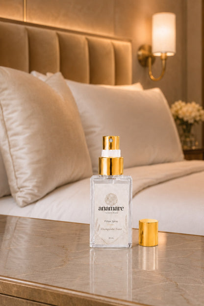 Pillow Spray Champanhe Toast 30 mL, frasco de vidro com válvula e tampa douradas, em quarto de hotel com cabeceira capitonê dourada, arandela acesa e bancada de mármore âmbar