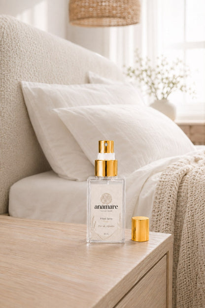 Pillow Spray Flor de Algodão 30 mL, frasco de vidro com válvula e tampa douradas, em quarto claro com cabeceira de bouclé, roupa de cama branca e manta de tricô, sobre criado-mudo de carvalho