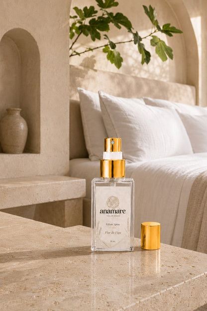 Pillow Spray Flor de Figo 30 mL, frasco de vidro com válvula e tampa douradas, em quarto de arquitetura mediterrânea com nicho em arco, galho de figueira e banco de pedra, sobre bancada de travertino