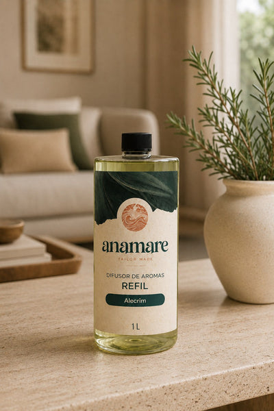 Refil de Difusor de Aromas Anamare de 1 litro, frasco transparente com tampa preta e rótulo verde-escuro com o selo da marca, sobre mesa de travertino em sala de estar, com sofá de linho, almofadas verdes e alecrim em vaso de cerâmica ao fundo