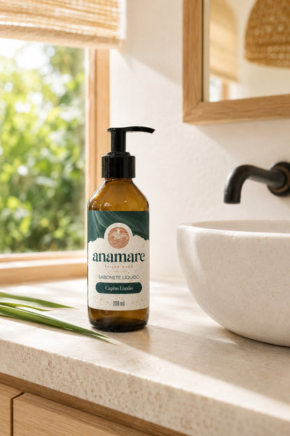 Sabonete Líquido para as Mãos Capim Limão 200 mL, frasco âmbar com válvula pump preta, em bancada de banheiro com cuba de pedra e a fragrância representada ao lado