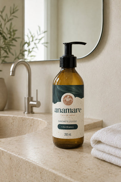 Sabonete Líquido para as Mãos Chá Branco 200 mL, frasco âmbar com válvula pump preta, em bancada de banheiro com cuba de pedra e a fragrância representada ao lado