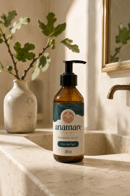 Sabonete Líquido para as Mãos Flor de Figo 200 mL, frasco âmbar com válvula pump preta, em bancada de banheiro com cuba de pedra e a fragrância representada ao lado