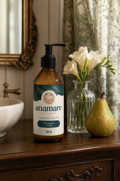 Sabonete Líquido para as Mãos Pera Inglesa e Frésia 200 mL, frasco âmbar com válvula pump preta, em bancada de banheiro com cuba de pedra e a fragrância representada ao lado