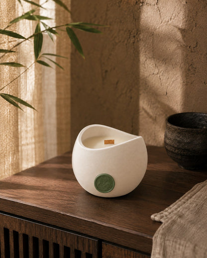 Vela Aromática Bambu Concreto 200 g em aparador de madeira escura, sob folhas de bambu