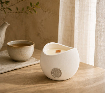 Vela Aromática Chá Branco Concreto 200 g em mesa de madeira clara, ao lado de bule e xícara de cerâmica
