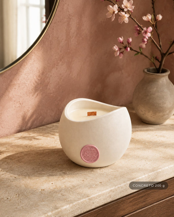 Vela Aromática Flor de Cerejeira Concreto 200 g em penteadeira, diante de parede rosada e ramo de cerejeira. Selo de tamanho no canto: CONCRETO 200 g
