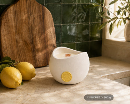 Vela Aromática Limão Siciliano Concreto 200 g em bancada de mármore, ao lado de limões-sicilianos e azulejo verde. Selo de tamanho no canto: CONCRETO 200 g