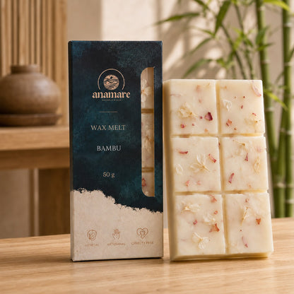 Wax Melt Anamare Bambu de 50 g, barra de cera vegetal com pétalas secas ao lado da caixa azul-petróleo com janela, em ambiente de ripado de madeira com cerâmica artesanal e bambu ao fundo, sobre mesa de carvalho
