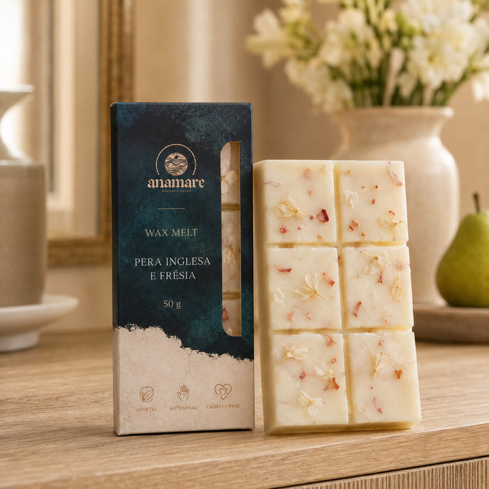 Wax Melt Anamare Pera Inglesa e Frésia de 50 g, barra de cera vegetal com pétalas secas ao lado da caixa azul-petróleo com janela, em aparador de madeira com moldura dourada, flores brancas em vaso de cerâmica e uma pera sobre travessa